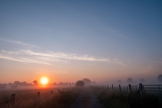 Misty Sunrise Over a Rural Country Path with Fence in Belgian Countryside