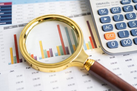 Magnifying glass and calculator resting on colorful financial charts with magnifying calculator business accounting analysis