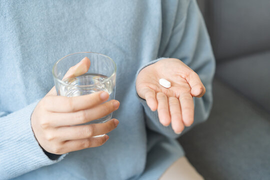 Sick, asian young woman, girl hand holding pill, painkiller medicine from stomach pain, headache, pain for treatment, take drug or vitamin and glass of water at home, pharmacy and health care concept.
