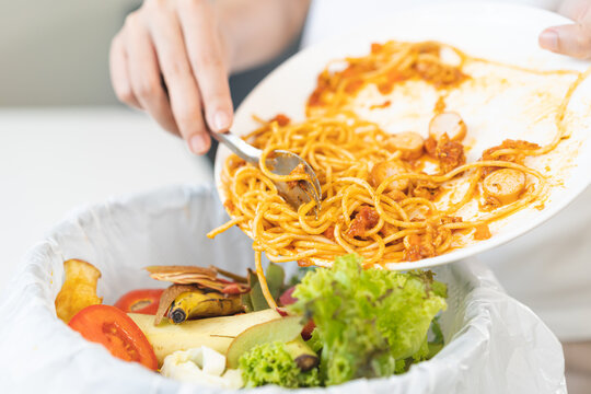 Compost from leftover food asian young housekeeper woman, female hand holding spaghetti plate use fork scraping waste, food throwing away into garbage, trash or bin. Environmentally responsible.
