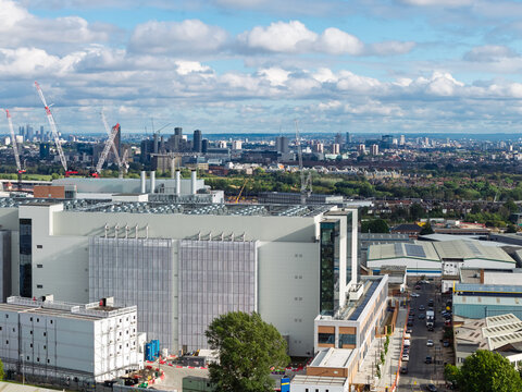 Aerial view of a large data center facility with industrial buildings, construction cranes, and a distant cityscape under a cloudy sky in the United Kingdom.