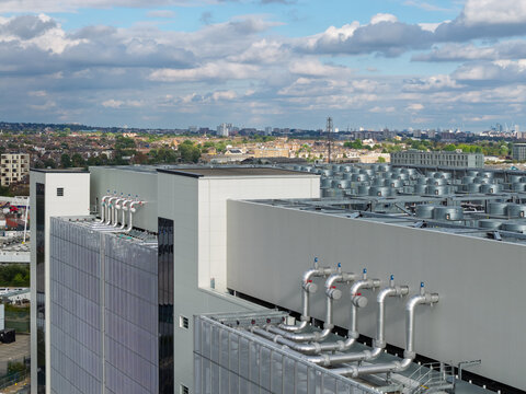 Aerial view of a modern data center building featuring rooftop cooling units and industrial piping with an urban cityscape in the United Kingdom.