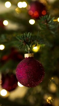 Detailed view of a beautiful holiday Christmas tree adorned with shiny red ornaments and warm golden garland lights blinking in soft focus bokeh.