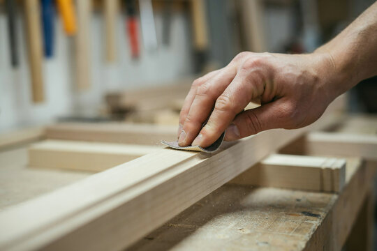 Carpenter hand sanding a wooden plank with sandpaper in a workshop