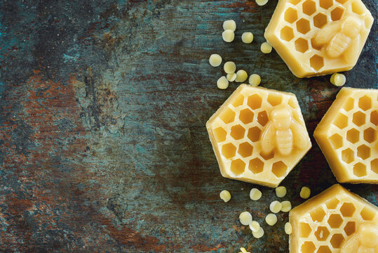 Honeycomb and bee shaped yellow beeswax blocks with wax pellets on rustic wooden  background.