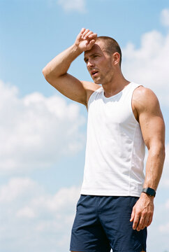 Young man wiping sweat from forehead after exercising outdoors  