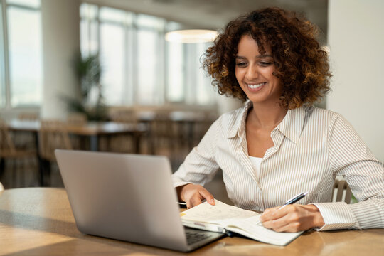 African business woman writing notes in notebook near laptop at coworking office workspace, planning. In 30s, female director works as founder, analyst, advisor, agent, banker, broker. Copy space
