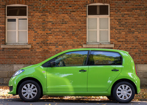 Wolfsburg, Germany - 14 Sep 2026: Bright green compact Skoda Citigo car parked parallel to a traditional red brick building facade on city street