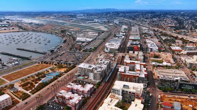 San Diego airport and waterfront transport corridors. Rail tracks and roads follow San Diego Bay past moored boats toward runways and airport buildings.