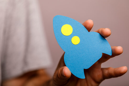 A hand holds a blue paper rocket, symbolizing business launch, innovation, and growth.