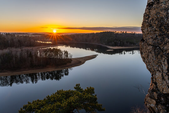 The sun sets over Sec Water reservoir, casting light on the water and trees. The sky shows warm colors and the surface reflects the scenery. A calm evening unfolds at this natural spot.