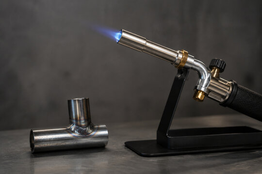Heavy-duty metal torch with blue flame and metal joint sample on display stand, practical preparedness and hardware tool concept