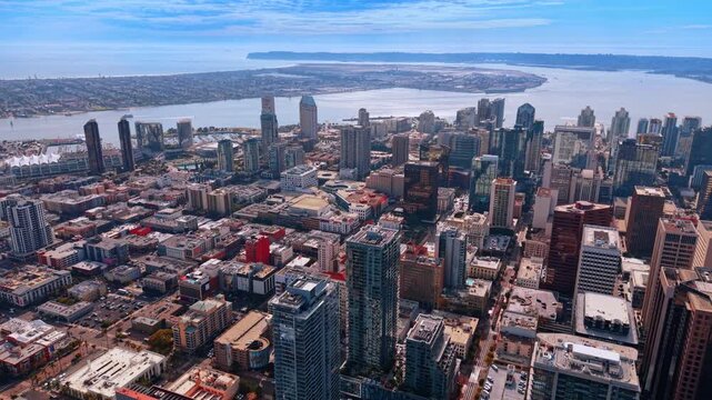 San Diego city blocks and waterfront towers above the bay. An elevated view shows streets and buildings extending toward San Diego Bay and its curved shoreline.