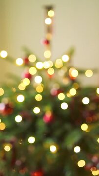 Abstract vertical shot of warm golden and red holiday garland lights blinking in heavy out of focus bokeh on a decorated Christmas tree. 