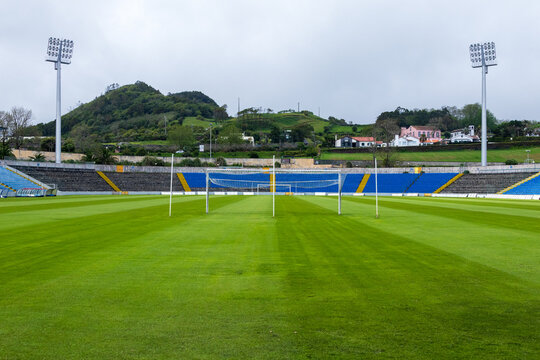 Perspectiva desde el terreno de juego del Estadio de S&atilde;o Miguel en Ponta Delgada, con sus gradas vac&iacute;as en tonos azules y las verdes colinas volc&aacute;nicas de fondo bajo un cielo nublado.
