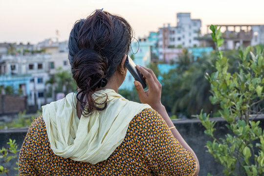 Woman standing on rooftop making a phone call with cityscape background. Outdoor cellular network communication and lifestyle view.