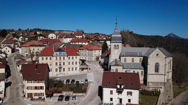 Aerial view of the historic Church of Saint-Maurice surrounded by traditional stone houses with red-tiled roofs in the village of Jougne, Bourgogne-Franche-Comte, France.