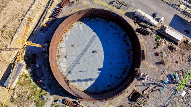 Aerial view of the assembly of a large circular oil storage tank at an industrial construction site with cranes and building materials in Kovin, Vojvodina, Serbia.