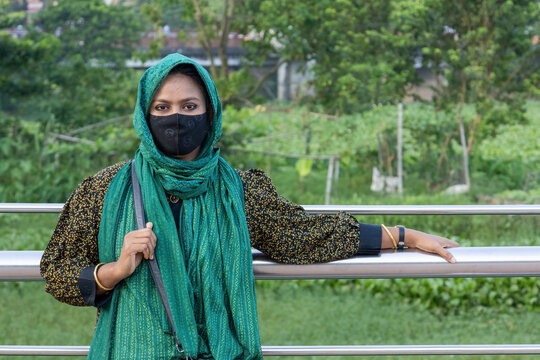 South Asian woman wearing green headscarf and protective mask leaning on railing. Muslim female modest fashion and outdoor lifestyle.