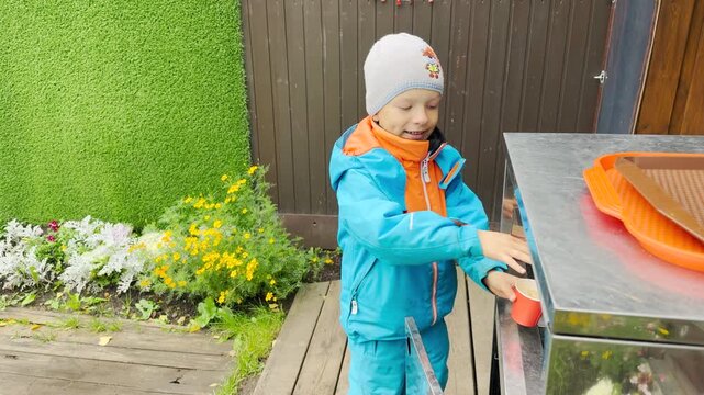 A cheerful boy reaches happily for a cup at an outdoor cafe stand. This joyful moment brings warm delight to Pavlovsk Park, Saint Petersburg.