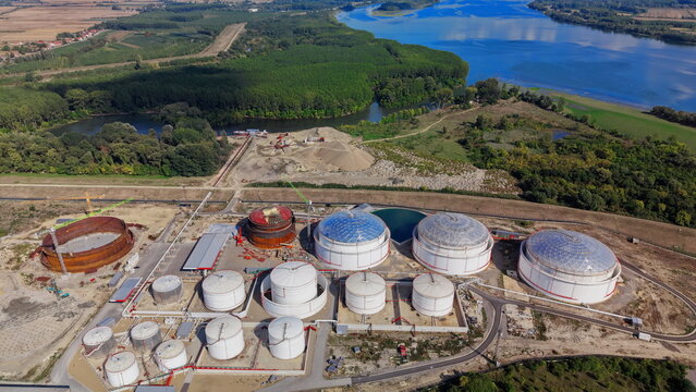 Aerial view of industrial fuel storage tanks with white spherical and cylindrical containers, a construction site with an empty tank shell, and greenery in Kovin, Vojvodina, Serbia.