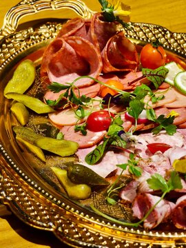 Cold cuts platter with pickles and vegetables on golden tray