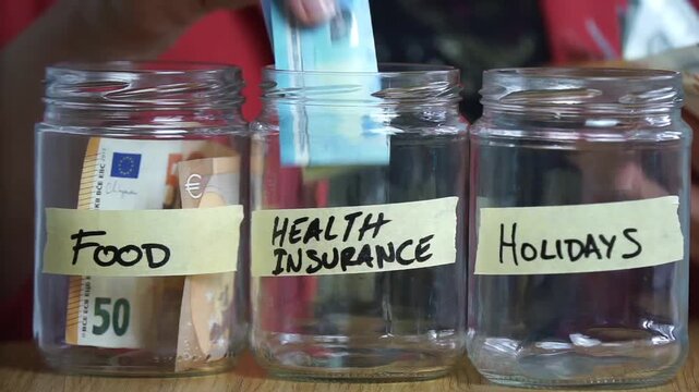Woman budgeting money by placing euro cash into three clear glass jars labeled Food, Health Insurance, and Holidays.