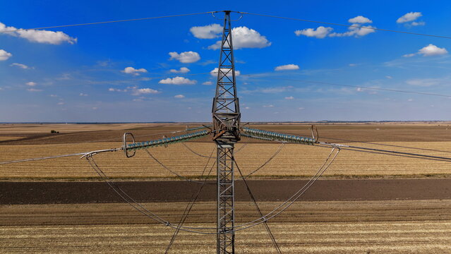 Aerial view of electric power transmission lines spanning across vast agricultural fields under a clear blue sky in Pancevo, Serbia.