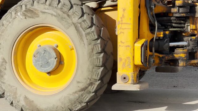 A heavy yellow excavator rests quietly near a dirt trench on a sunny street. Its powerful presence brings a feeling of steady industrial progress and calm focus to the city work site.