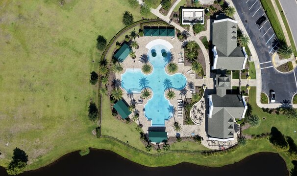 Aerial view of the Windward Ranch swimming pool complex featuring a uniquely shaped pool, surrounding palm trees, clubhouse, and green lawns in St. Johns County, Florida, United States.