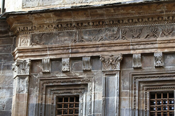 Ornate historic stone building facade with carved architectural details, weathered surface, decorative cornice, barred windows, and aged textures on old urban heritage structure © Ivan