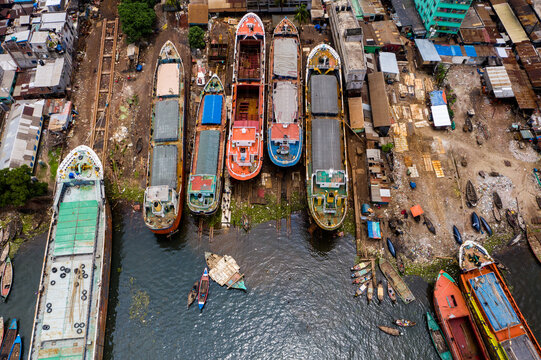 Aerial view of a busy shipyard with multiple cargo ships docked for maintenance and repair, surrounded by industrial buildings and urban infrastructure in Dhaka, Dhaka Division, Bangladesh.