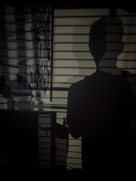 Dark shadow anonymous self-portrait in front of window blinds at night