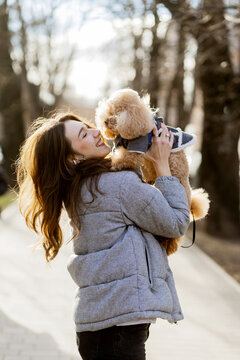 Outdoor winter portrait of happy woman holding her brown poodle dog