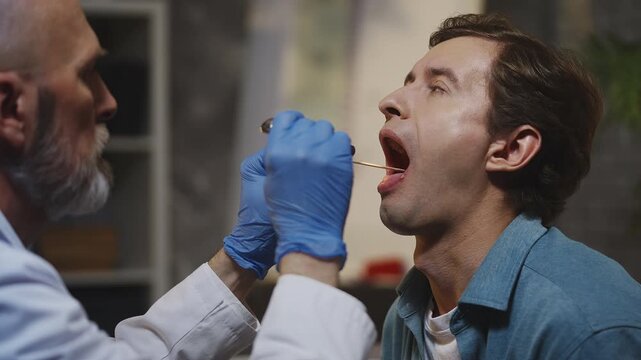 Doctor inspects male patient's throat during ENT consultation in office