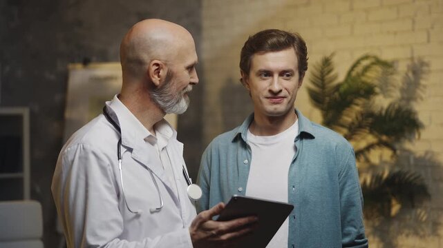 Doctor explains medical test results on tablet to male patient at check-up