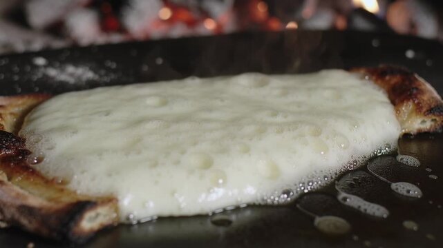 Melting thick white cheese bubbling under heat from coals on griddle, with charred flatbread