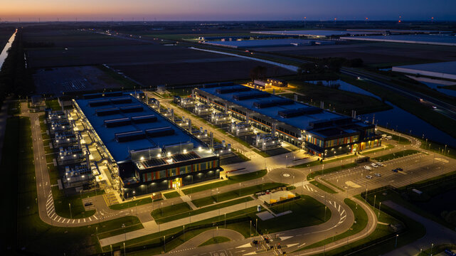 Aerial view of the Microsoft data center illuminated at night with surrounding parking lots, roads, and agricultural fields in Middenmeer, North Holland, Netherlands.