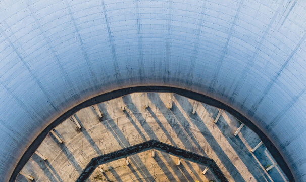 Aerial view of the interior of an abandoned concrete cooling tower at a power plant, featuring circular support columns and long evening shadows in Trino, Piedmont, Italy.