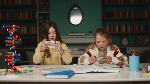 Two excited sisters play on their smartphones instead of doing homework