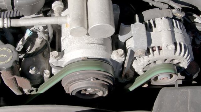 Detail shot of a large 8 cylinder diesel engine running with belts, alternator, and compressor turning.
