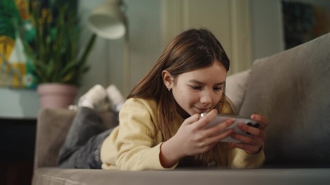 A girl plays on smartphone while lying on sofa, gadget dependency concept