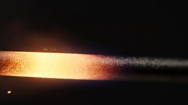 Burning matchstick flickers in a dark setting with glowing ember, smoke, and sparks. Fire safety campaigns, combustion education, and energy presentations.