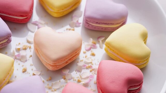 Colorful heart-shaped macarons rest on a white plate in a close-up pastel dessert arrangement. Bakery advertising, dessert menu promotion, and confectionery packaging.