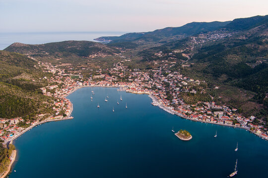Aerial view of the town of Vathy on Ithaca island, featuring a deep blue bay with sailboats, surrounded by lush green hills and Mediterranean architecture in Ithaki, Greece.