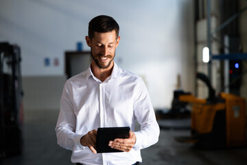 Man smiling, using a digital tablet for inventory management and logistics planning inside a modern industrial warehouse © Dejan