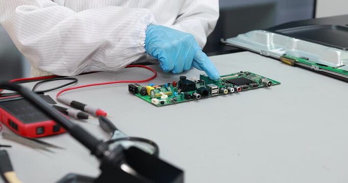 Electronics technician in a clean work area testing circuit boards with probes and multimeter equipment during device repair and quality inspection.