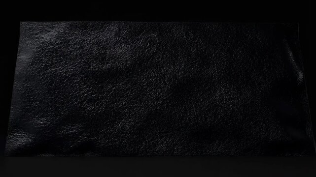 Close-up black textured surface wrinkles and folds under subtle lighting. Abstract backdrop shaped by surface deformation, material texture and surface detail.