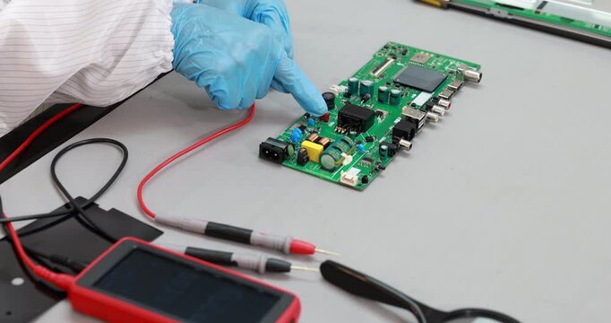 Technician wearing blue gloves tests and repairs a green circuit board with multimeter probes on a workbench.