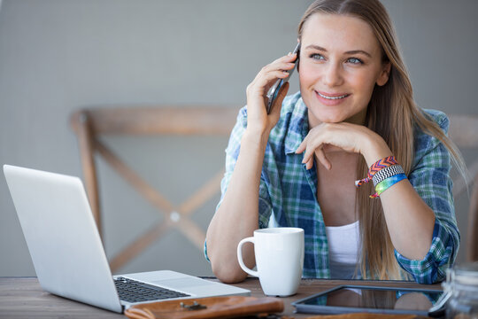 Young Woman Working on Laptop and Talking on Phone